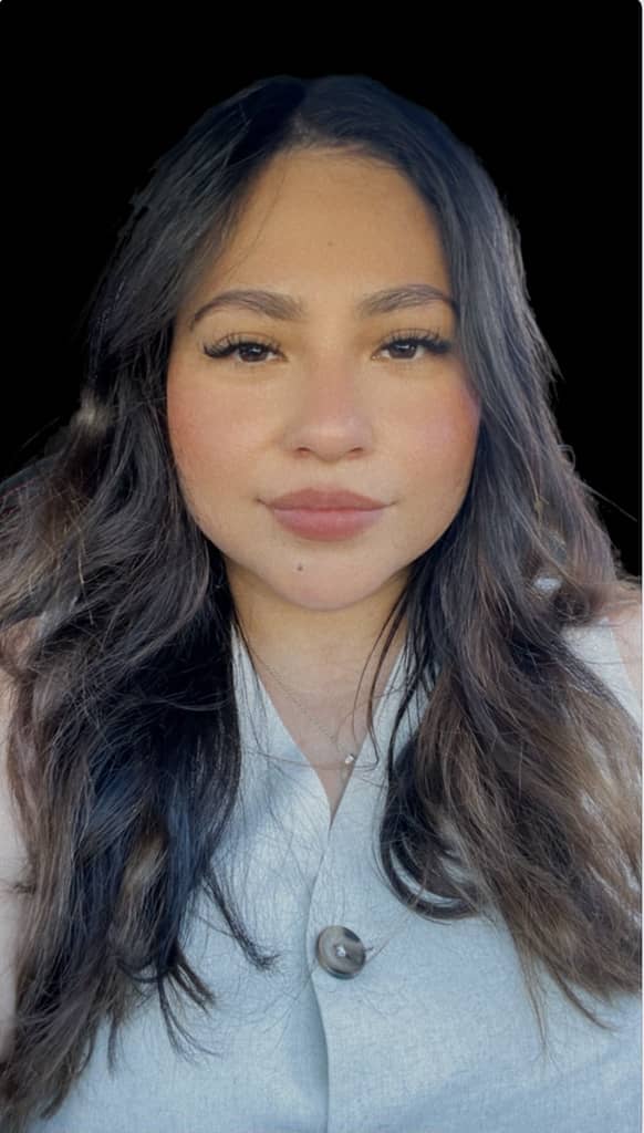 mayra looking into the camera with a soft smile. She is wearing a silk copper shirt and makeup